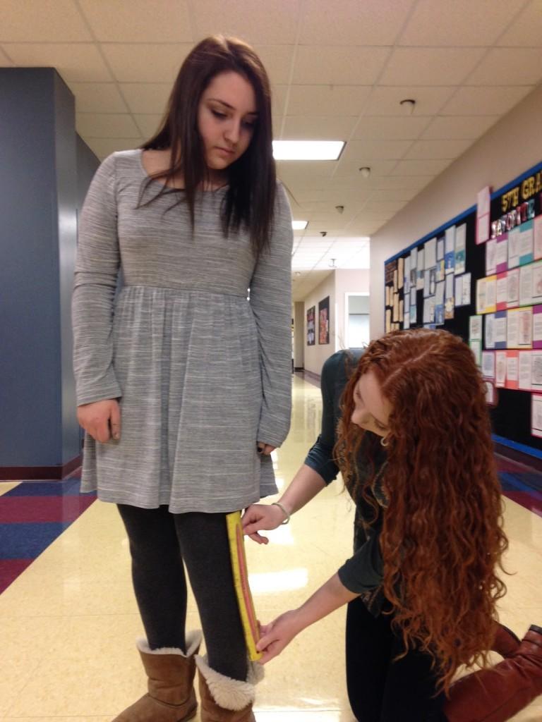 Sophomore Leah Sosland  measures the length of freshman Amanda Sokols dress. Its long enough! Photo by Alexis Davis.