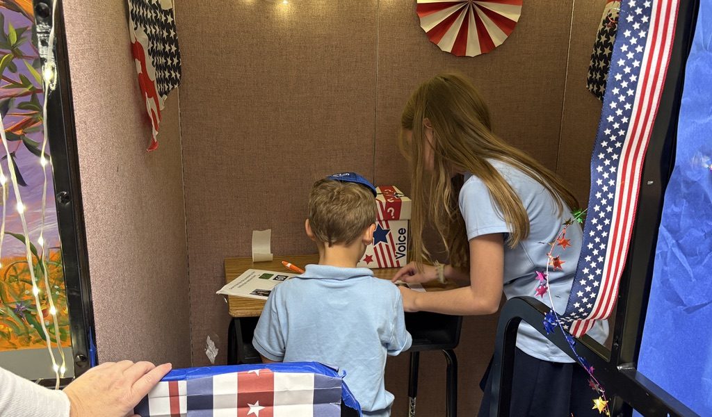 The fifth graders took turns standing inside the voter box helping the kindergartners read their choices for who they could vote for. Photo by Elia Ellis
